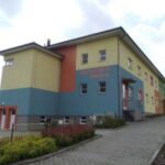 Mateřská škola v Humpolci s pastelově zbarvenou fasádou a jehličnany před budovou