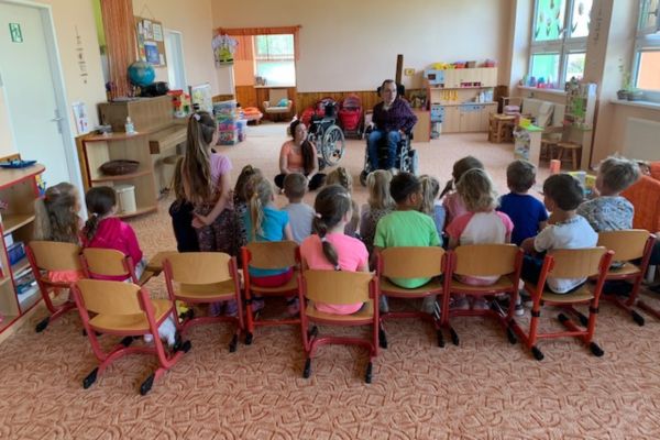 Skupina dětí v mateřské škole naslouchá besedě s lektory na vozíku