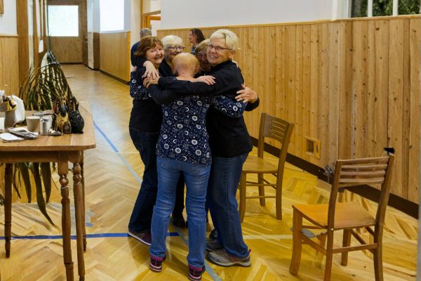 Skupina žen se objímá v kruhu během setkání. Fotografie vyjadřuje vzájemnou podporu, radost ze společenství a propojení, které jsou součástí inkluzivního přístupu projektu Ekvilibro.